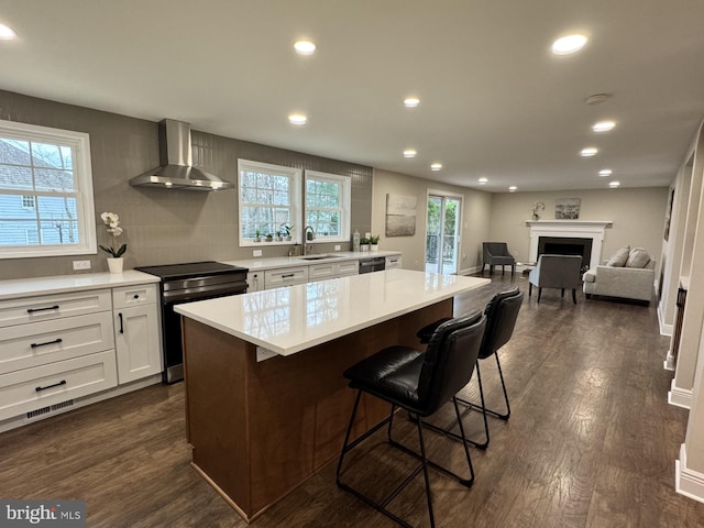 kitchen featuring dark wood-type flooring, a breakfast bar, electric stove, wall chimney exhaust hood, and a sink