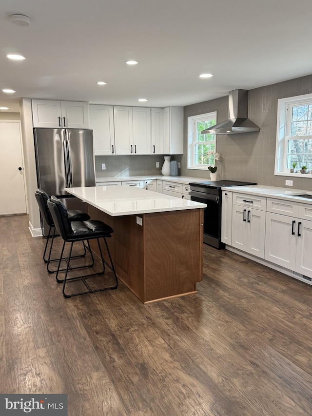 kitchen featuring dark wood-style floors, a kitchen island, freestanding refrigerator, electric stove, and wall chimney range hood