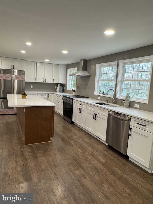 kitchen with a sink, stainless steel appliances, dark wood-type flooring, light countertops, and wall chimney exhaust hood