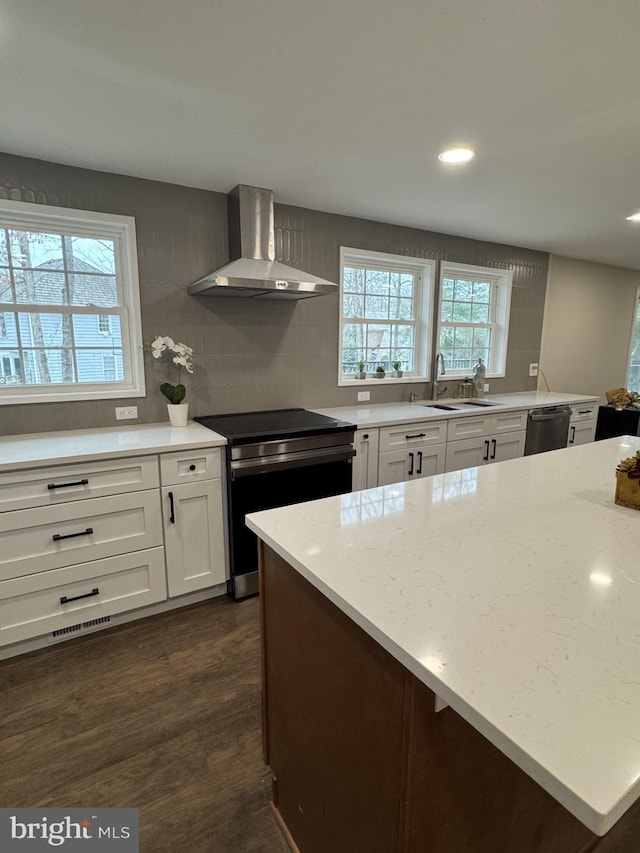 kitchen featuring wall chimney range hood, dishwashing machine, stainless steel range with electric stovetop, white cabinets, and a sink