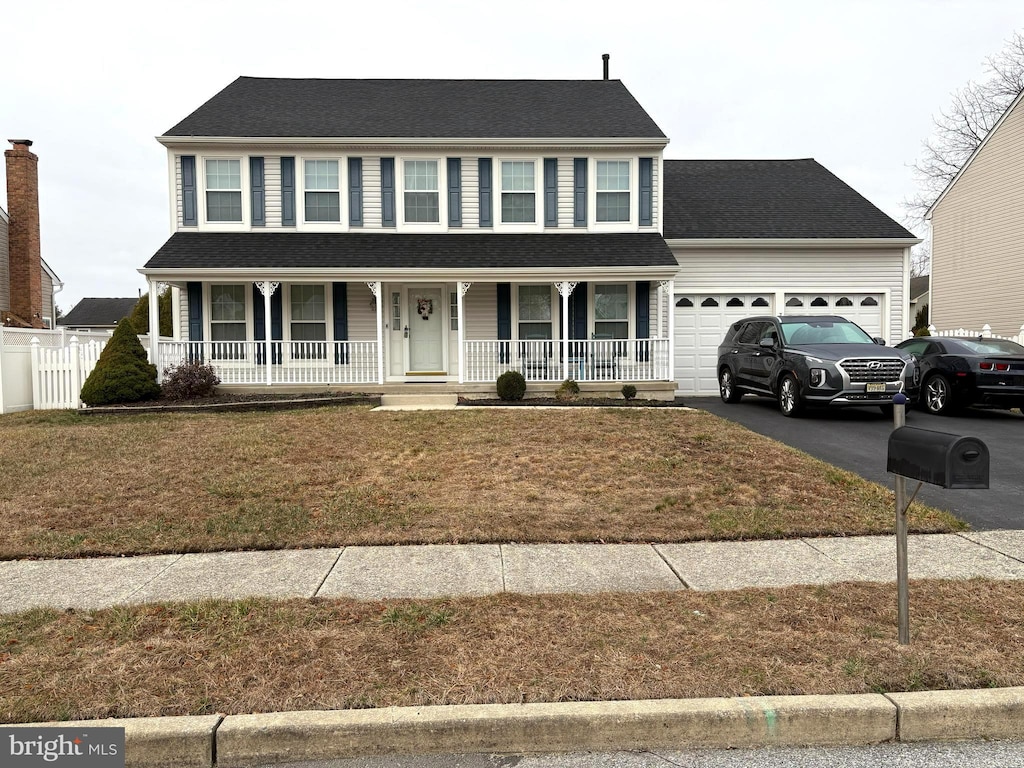 colonial home featuring aphalt driveway, a porch, a front yard, and an attached garage