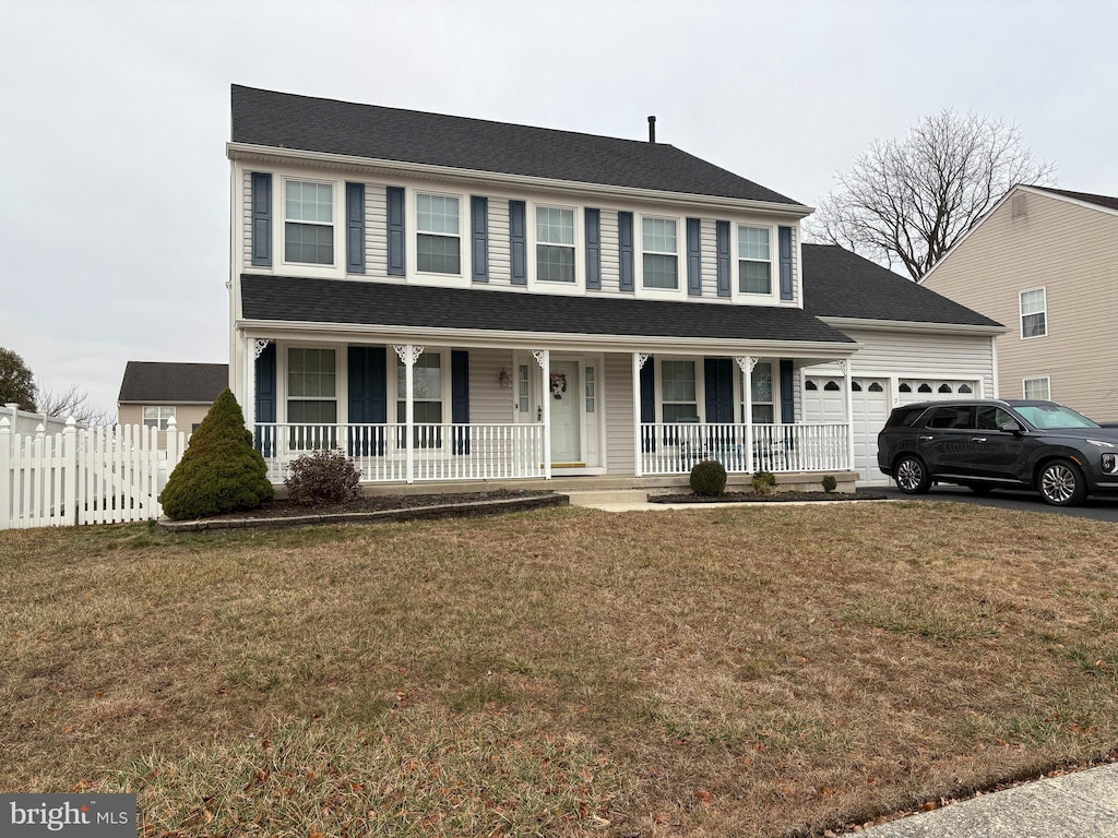 colonial inspired home featuring driveway, a front lawn, fence, covered porch, and a garage