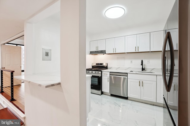 kitchen featuring light stone counters, a sink, under cabinet range hood, appliances with stainless steel finishes, and marble finish floor