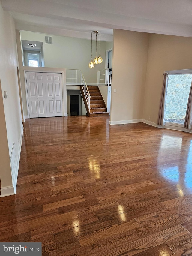 unfurnished living room featuring visible vents, baseboards, wood finished floors, and stairs