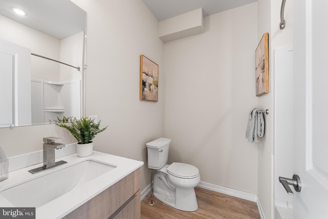 bathroom with toilet, wood finished floors, baseboards, walk in shower, and vanity