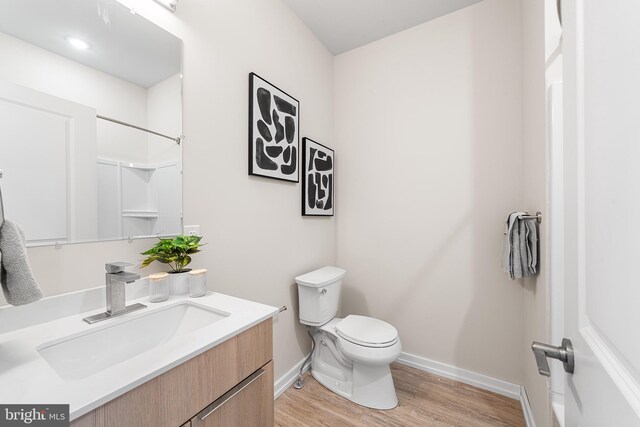 bathroom with vanity, toilet, wood finished floors, and baseboards
