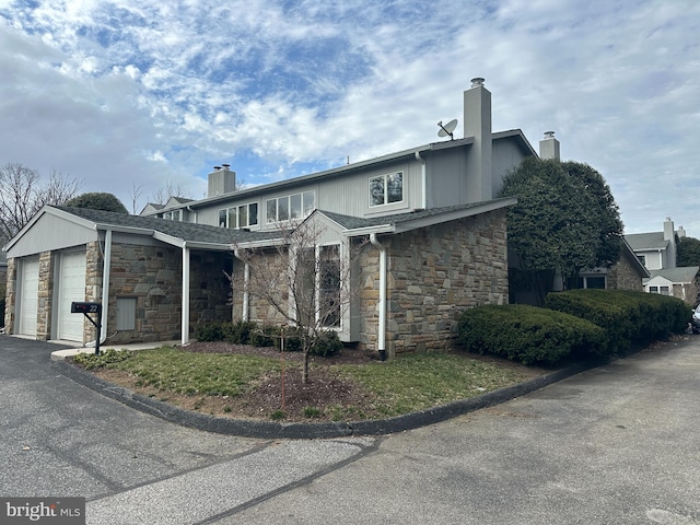 view of front of house with driveway, stone siding, an attached garage, and a chimney