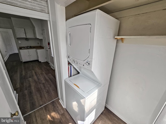 clothes washing area with dark wood finished floors, baseboards, stacked washer / drying machine, and a sink