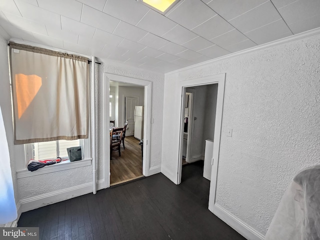 interior space featuring a textured wall, dark wood-style flooring, freestanding refrigerator, and ornamental molding