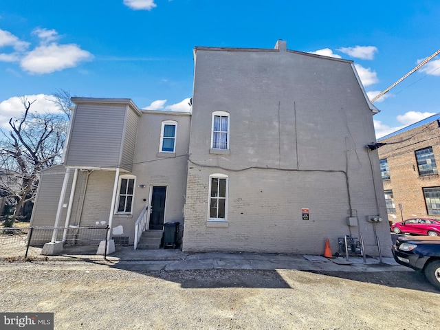 rear view of house featuring entry steps, fence, and brick siding