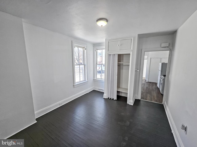 unfurnished bedroom with dark wood-style floors, a closet, freestanding refrigerator, and baseboards