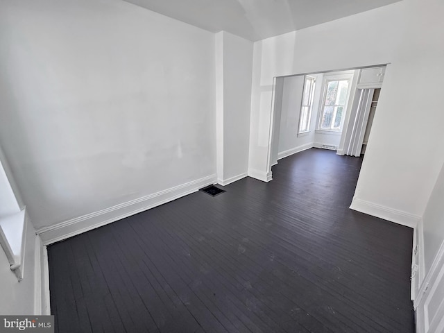 spare room with visible vents, baseboards, and dark wood-style flooring