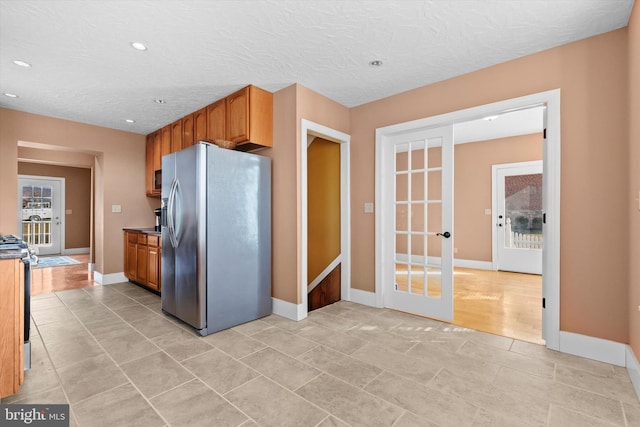 kitchen featuring baseboards, stainless steel fridge, a textured ceiling, and black range oven