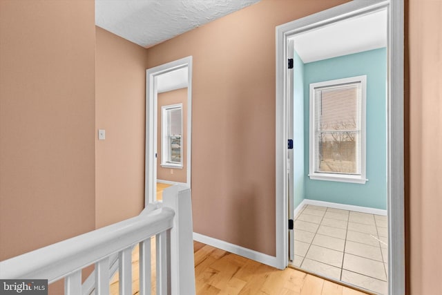 hall featuring light wood-type flooring, baseboards, and a textured ceiling