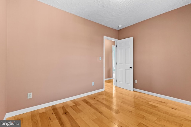 spare room featuring light wood-style flooring, baseboards, and a textured ceiling