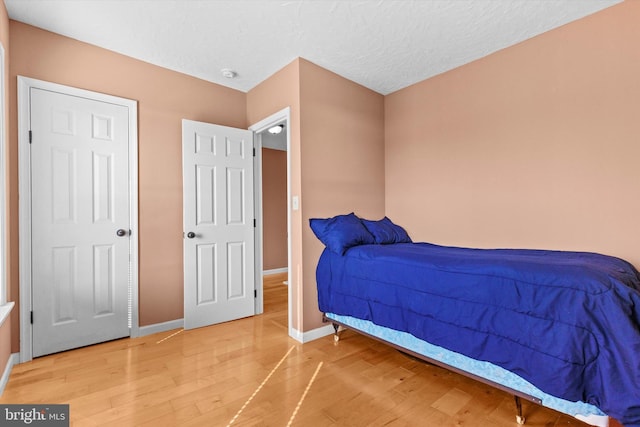 bedroom featuring light wood-type flooring, baseboards, and a textured ceiling