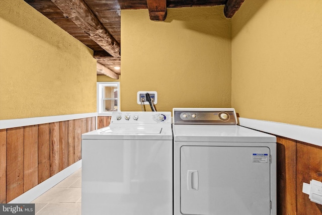 clothes washing area with a wainscoted wall, washing machine and dryer, wooden walls, tile patterned flooring, and wood ceiling