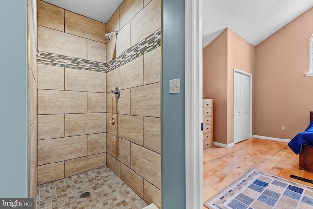 full bath with baseboards, wood finished floors, and a tile shower