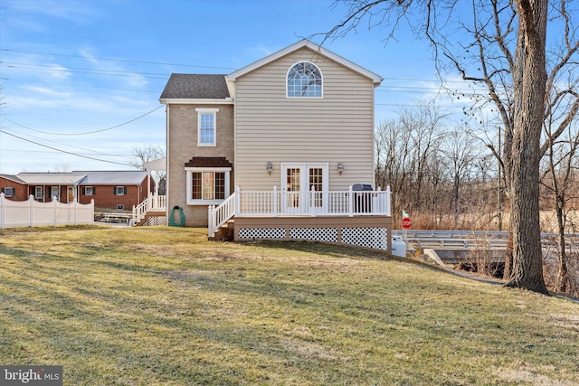 rear view of house with a lawn, a wooden deck, roof with shingles, and fence