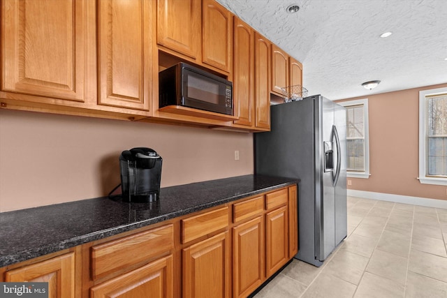 kitchen with brown cabinetry, stainless steel fridge, black microwave, and a textured ceiling