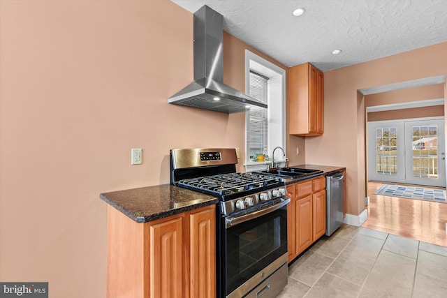 kitchen featuring light tile patterned floors, appliances with stainless steel finishes, a textured ceiling, wall chimney exhaust hood, and a sink