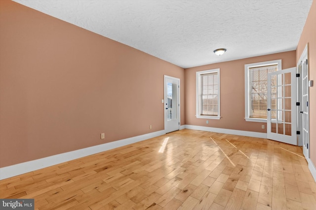 unfurnished room featuring baseboards, light wood-type flooring, and a textured ceiling