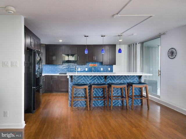 kitchen with a kitchen breakfast bar, a kitchen island, wood finished floors, freestanding refrigerator, and light countertops