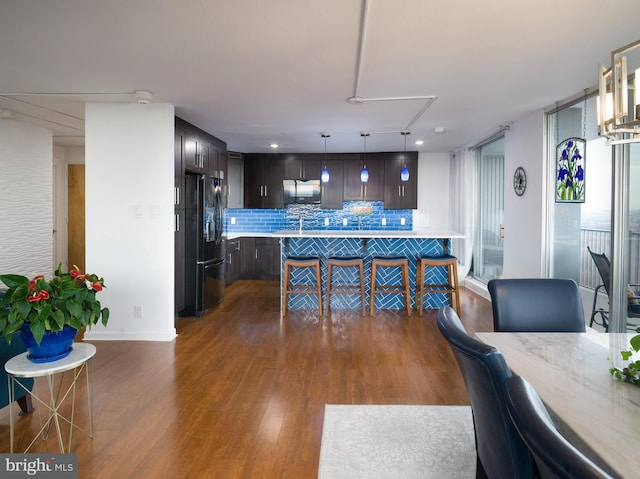 kitchen featuring backsplash, dark brown cabinetry, a breakfast bar area, black fridge with ice dispenser, and dark wood-style flooring