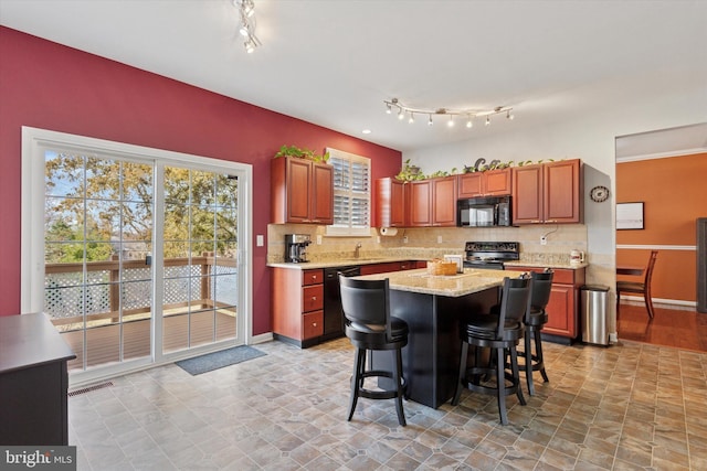 kitchen featuring black appliances, a breakfast bar, a kitchen island, tasteful backsplash, and light stone countertops