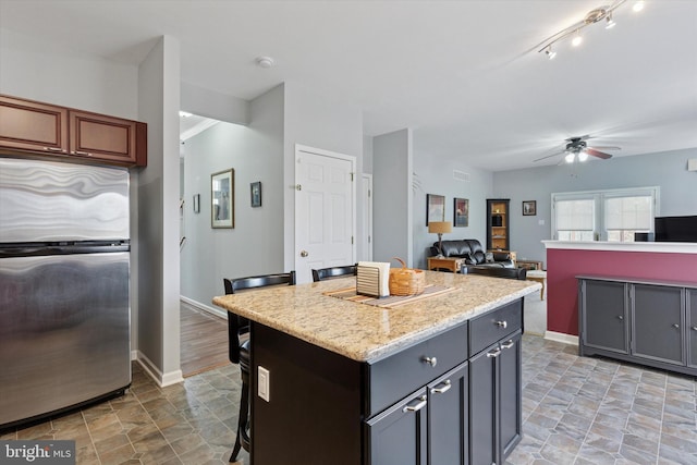 kitchen featuring a kitchen island, baseboards, a kitchen bar, freestanding refrigerator, and a ceiling fan