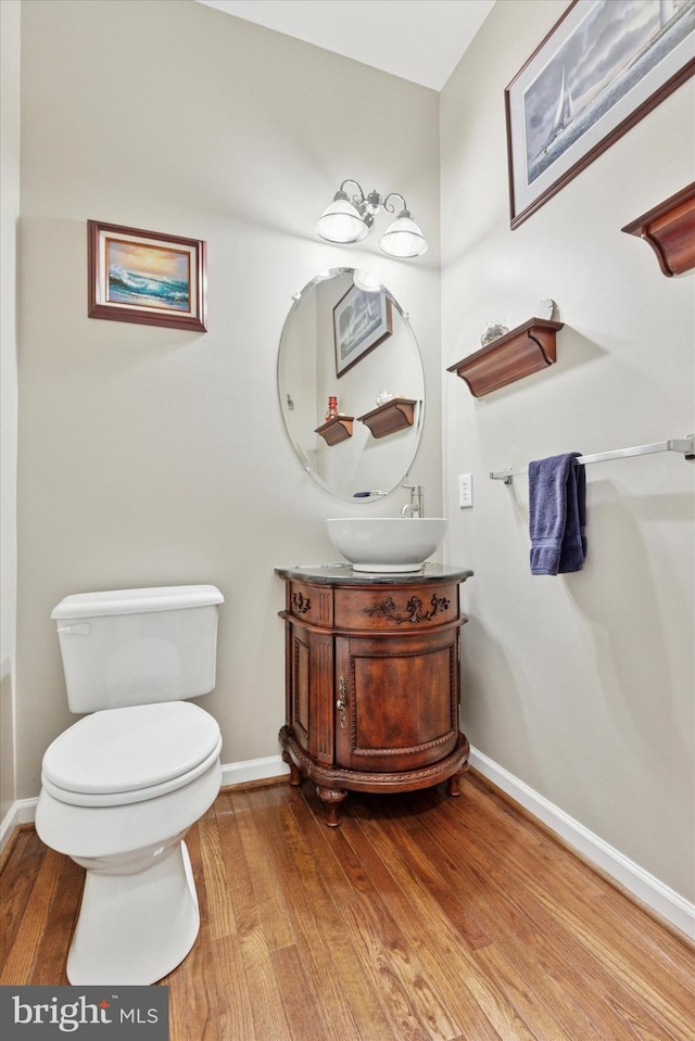 half bathroom featuring vanity, toilet, wood finished floors, and baseboards