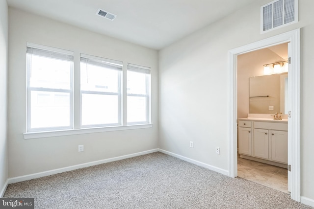 unfurnished bedroom with connected bathroom, baseboards, visible vents, and light carpet