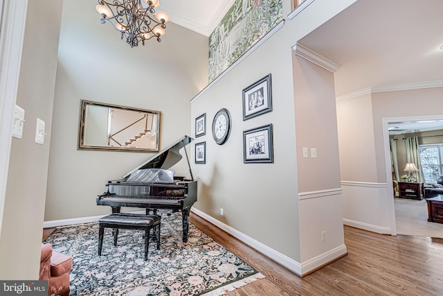 sitting room featuring wood finished floors, baseboards, a high ceiling, ornamental molding, and a notable chandelier