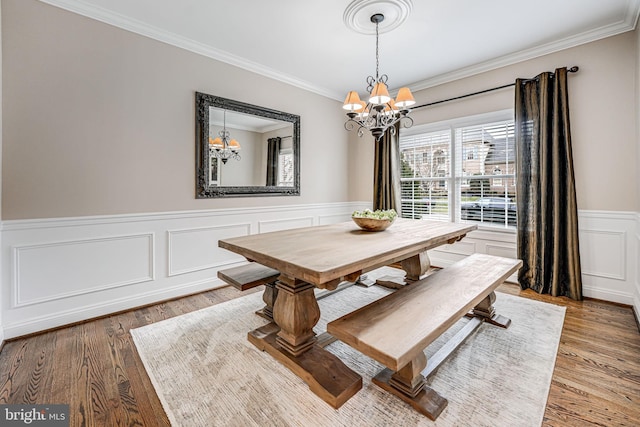 dining area featuring a wainscoted wall, light wood-type flooring, an inviting chandelier, and ornamental molding