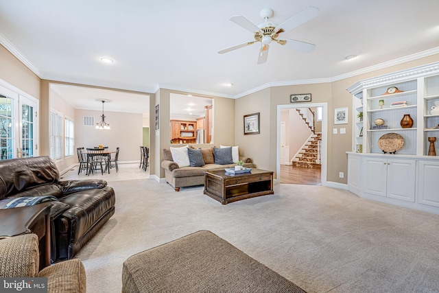 living area with visible vents, ornamental molding, ceiling fan with notable chandelier, light colored carpet, and stairs