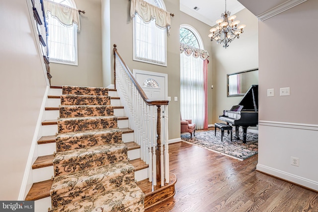 staircase featuring a chandelier, ornamental molding, a healthy amount of sunlight, and wood finished floors