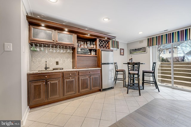 bar featuring light tile patterned floors, visible vents, freestanding refrigerator, bar, and tasteful backsplash