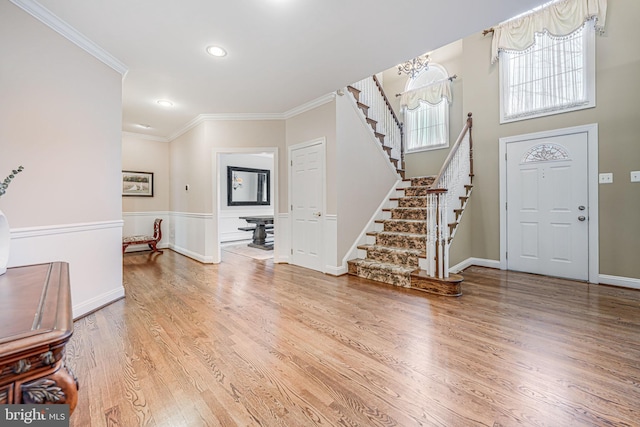 foyer with stairway, wood finished floors, ornamental molding, wainscoting, and a notable chandelier