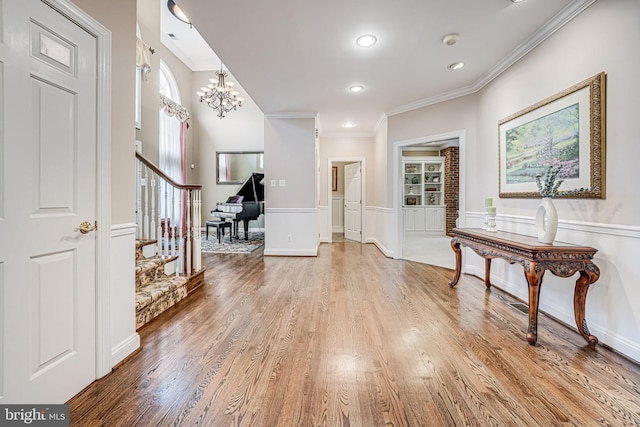 entryway featuring a notable chandelier, stairs, light wood-style floors, and ornamental molding