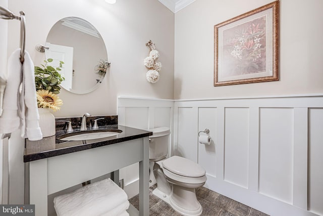 bathroom featuring a wainscoted wall, toilet, crown molding, a decorative wall, and vanity