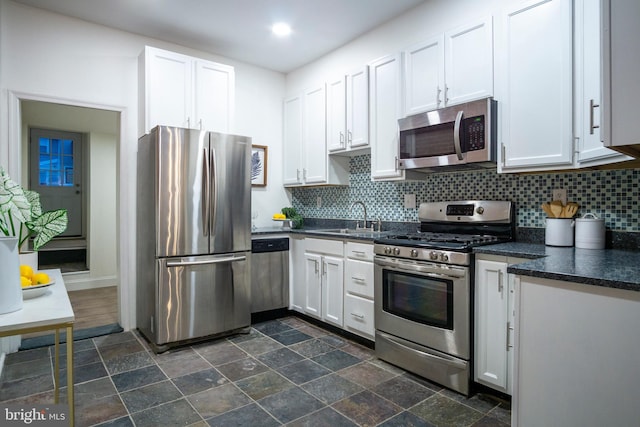 kitchen with dark countertops, white cabinets, appliances with stainless steel finishes, and a sink