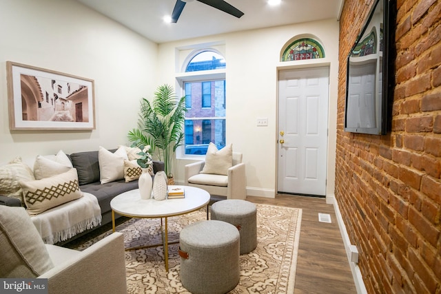 living area featuring a ceiling fan, wood finished floors, baseboards, and brick wall