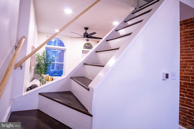 stairs with a ceiling fan and brick wall