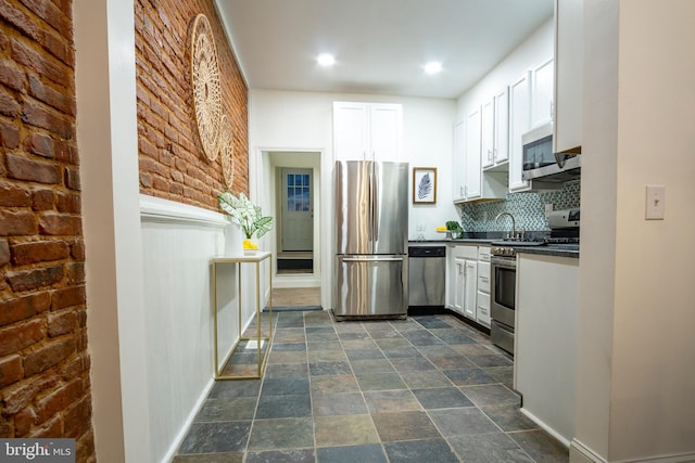 kitchen featuring stone finish floor, tasteful backsplash, dark countertops, stainless steel appliances, and white cabinets