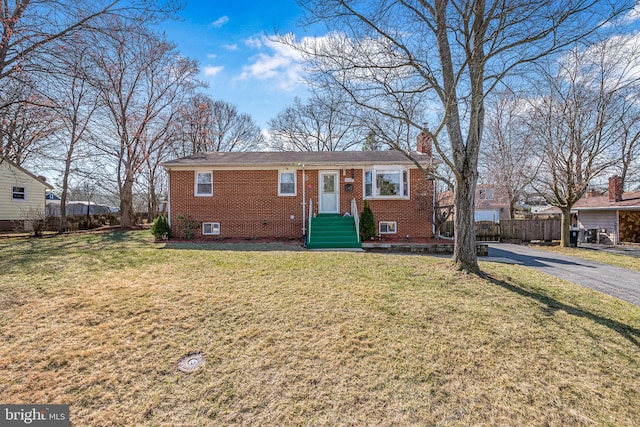 single story home featuring a front yard, fence, driveway, a chimney, and brick siding