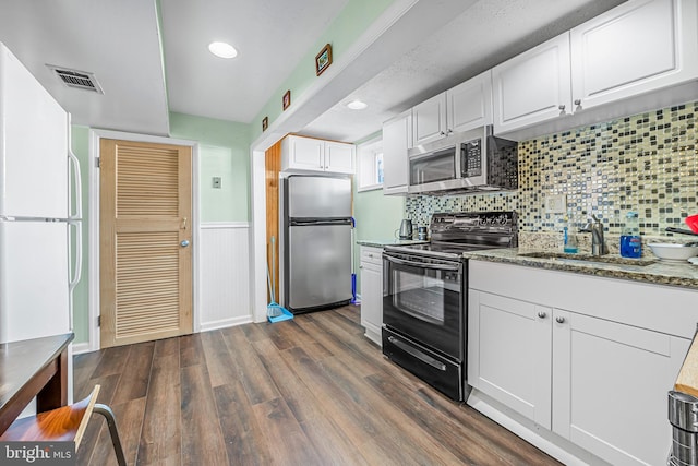 kitchen featuring dark wood-style floors, a wainscoted wall, visible vents, stainless steel appliances, and white cabinets