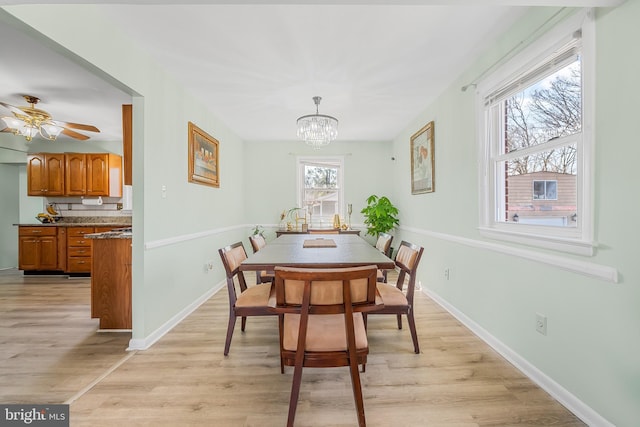 dining area featuring ceiling fan with notable chandelier, baseboards, and light wood-style floors