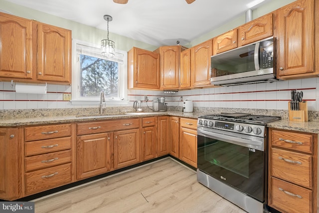 kitchen with backsplash, light stone countertops, decorative light fixtures, stainless steel appliances, and a sink