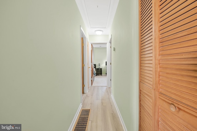 hallway featuring attic access, light wood-style floors, baseboards, and visible vents