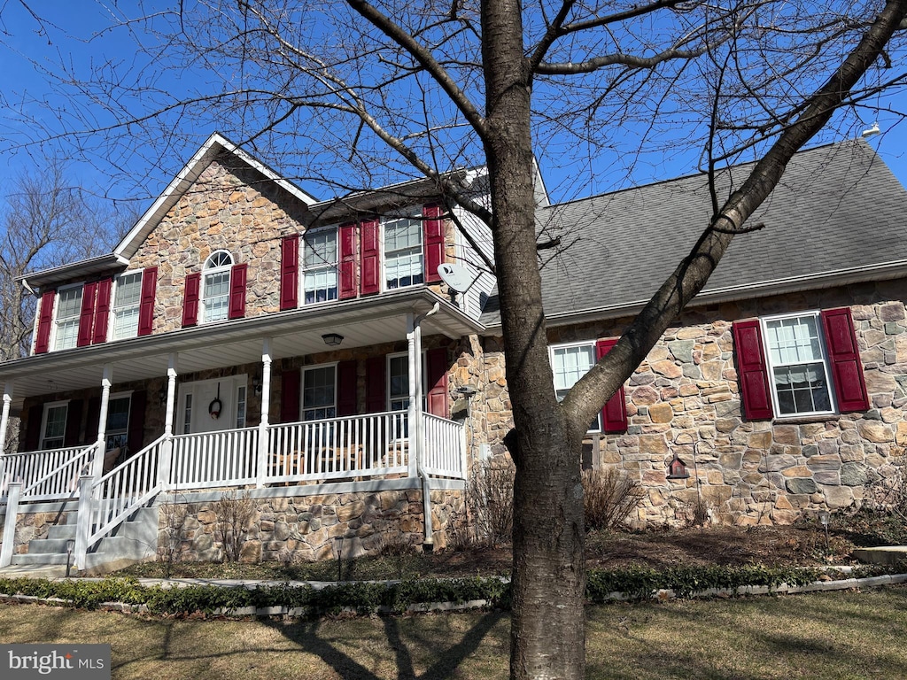 colonial home featuring stone siding, a porch, and roof with shingles